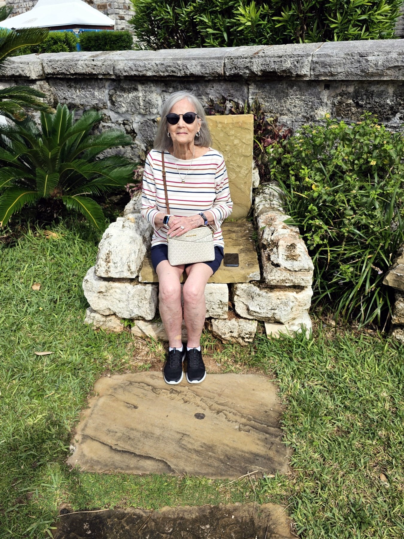 Ann Filipone seated outdoors on a stone chair in the sunshine