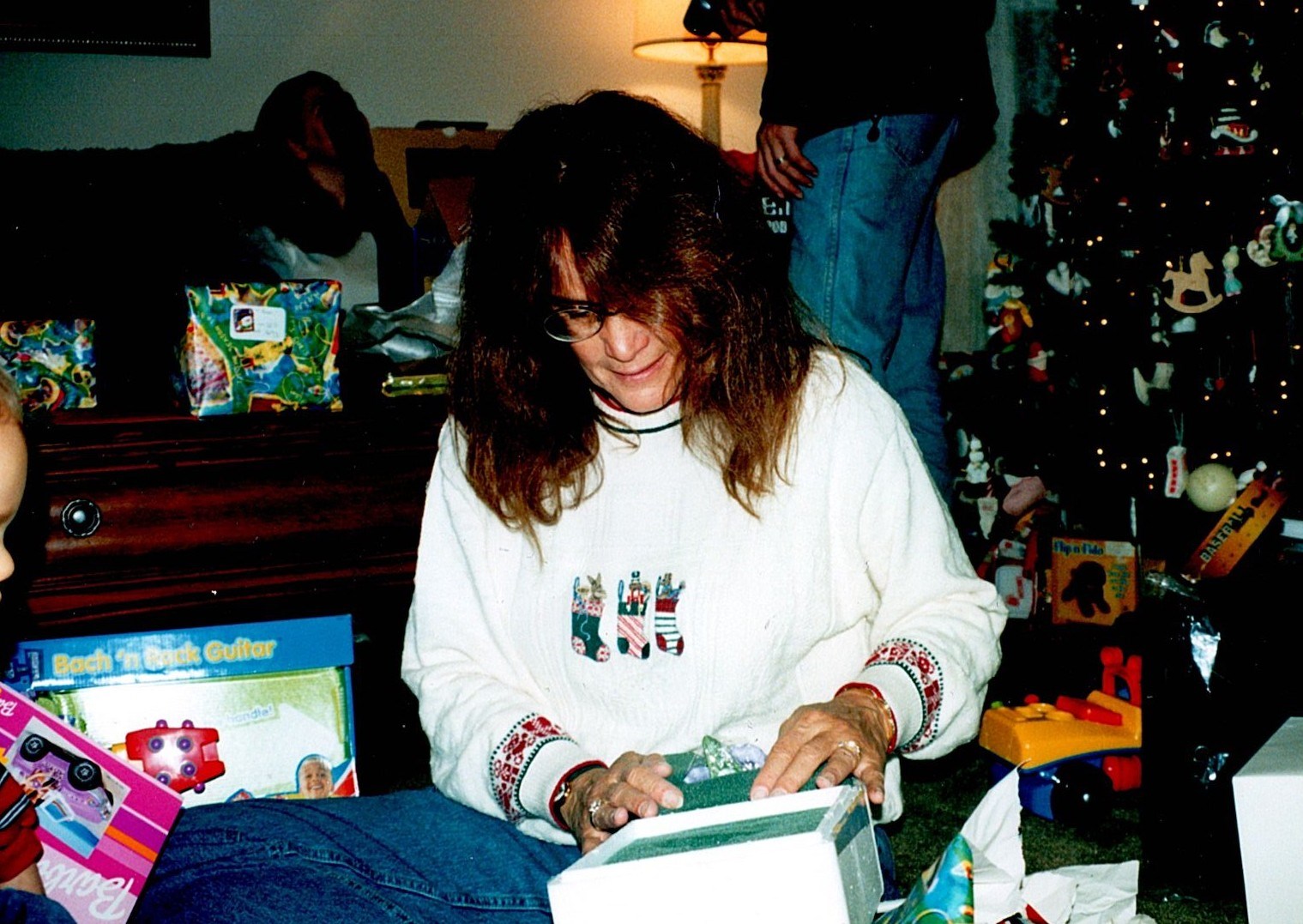 Ann Filipone opening a Christmas gift on the floor beside a tree